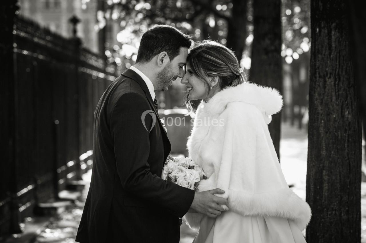 Un couple de mariés se tient face à face dans une rue bordée d'arbres, éclairée par une lumière douce.