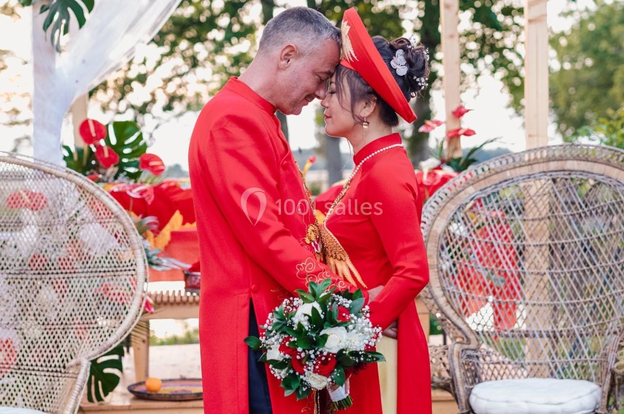 Un couple en tenue traditionnelle rouge se tient tête contre tête lors d'une cérémonie en extérieur.