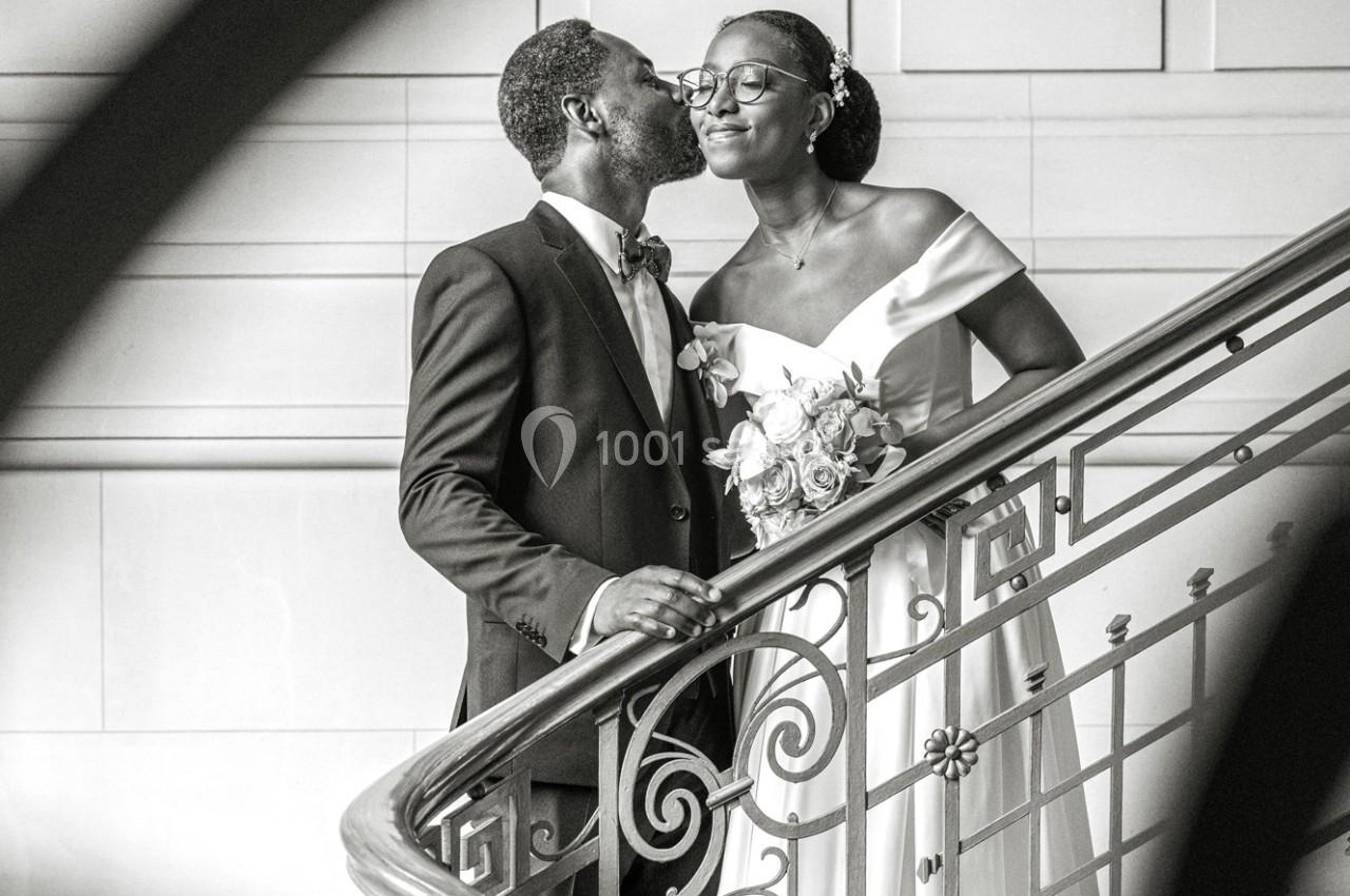 Un couple habillé élégamment partage un moment complice sur un escalier en intérieur.