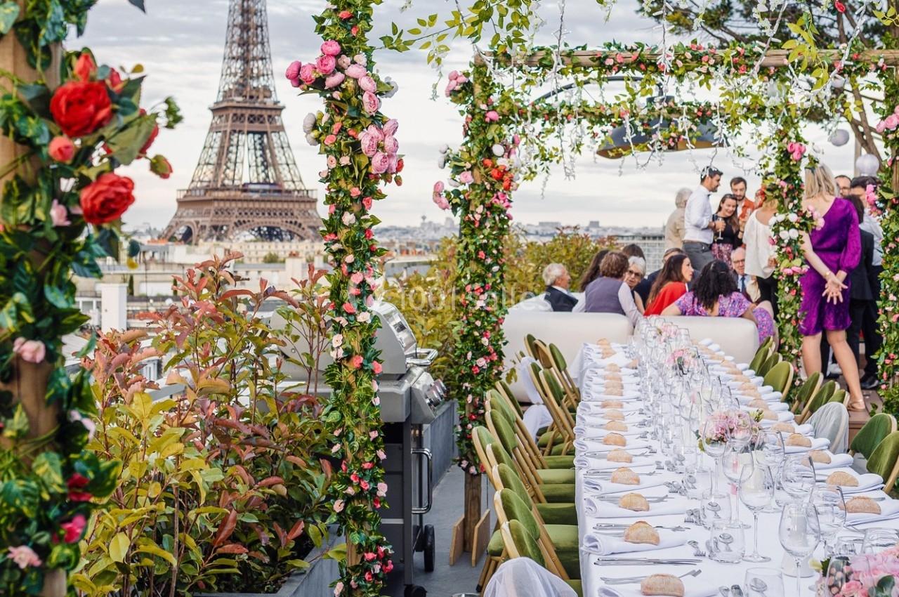 Table dressée pour un repas en extérieur avec vue sur la Tour Eiffel, entourée de végétation et de fleurs.