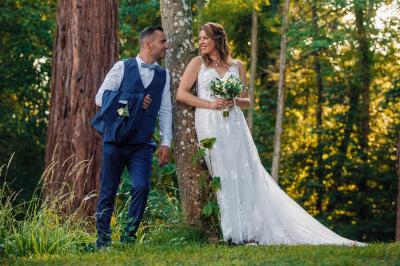 Un couple en tenue de mariage pose dans une forêt verdoyante, éclairée par une lumière douce.
