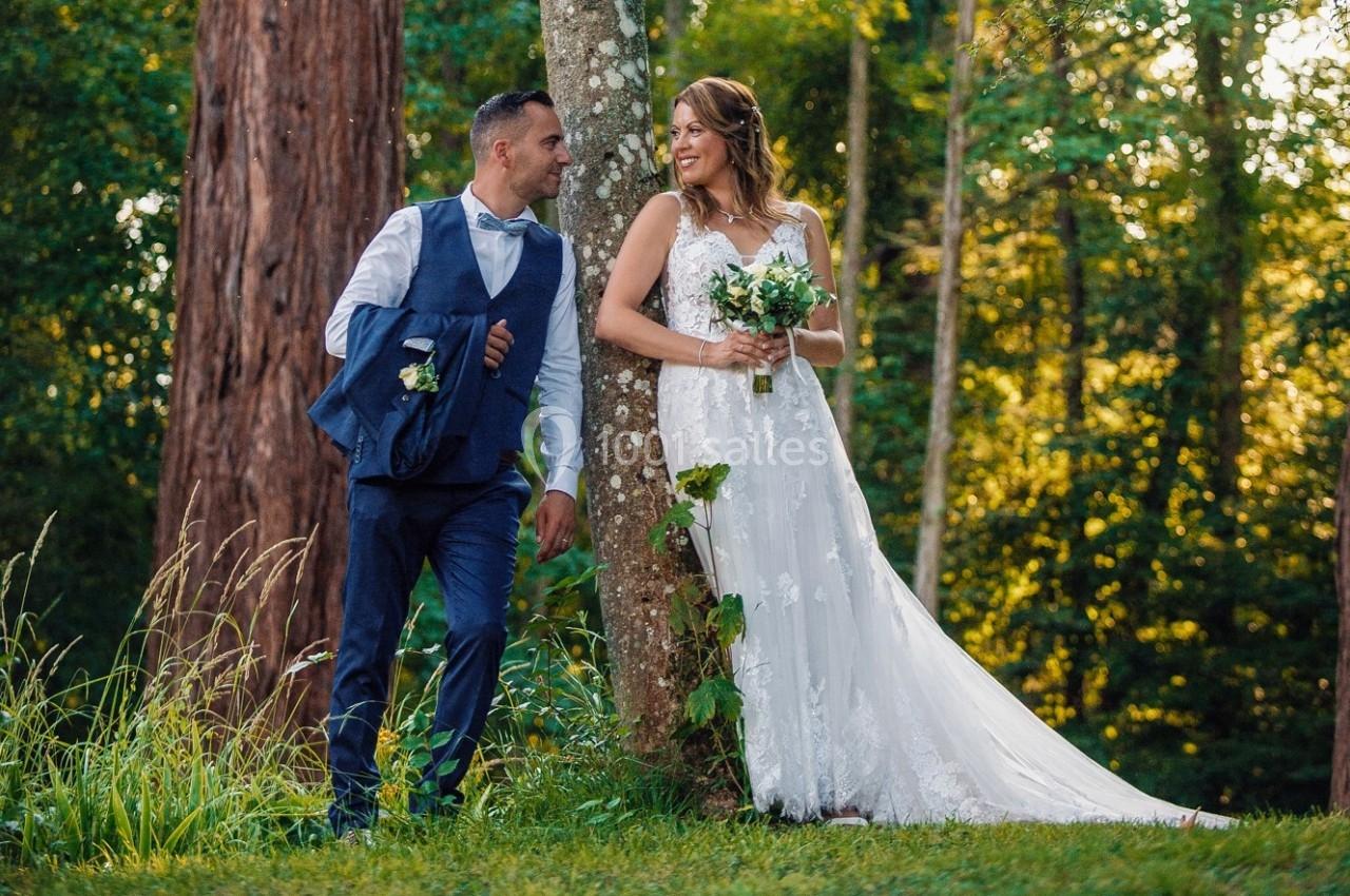 Un couple en tenue de mariage pose dans une forêt verdoyante, éclairée par une lumière douce.