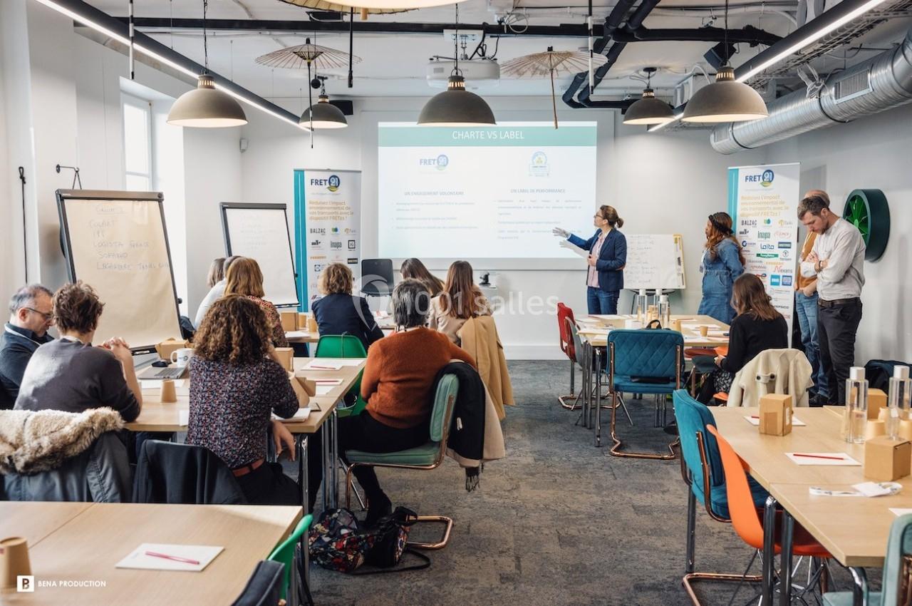 Un groupe de personnes assiste à une présentation dans une salle de réunion moderne avec écran et tableaux.