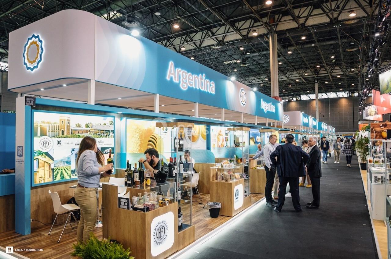 Stand de l'Argentine dans un salon, avec des visiteurs discutant et des produits exposés sur des comptoirs en bois.