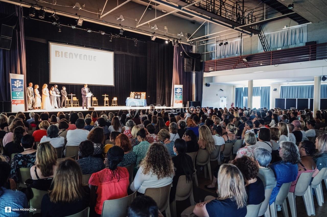 Une assemblée de personnes assises dans une salle de spectacle, face à une scène où se tient une présentation.