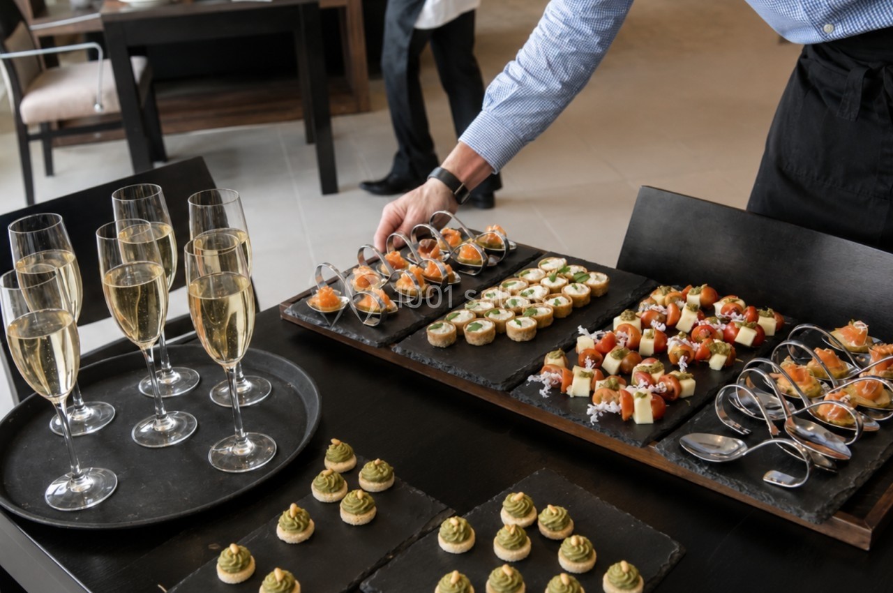 Plateau de bouchées apéritives variées avec flûtes de champagne sur une table, préparé pour un événement.