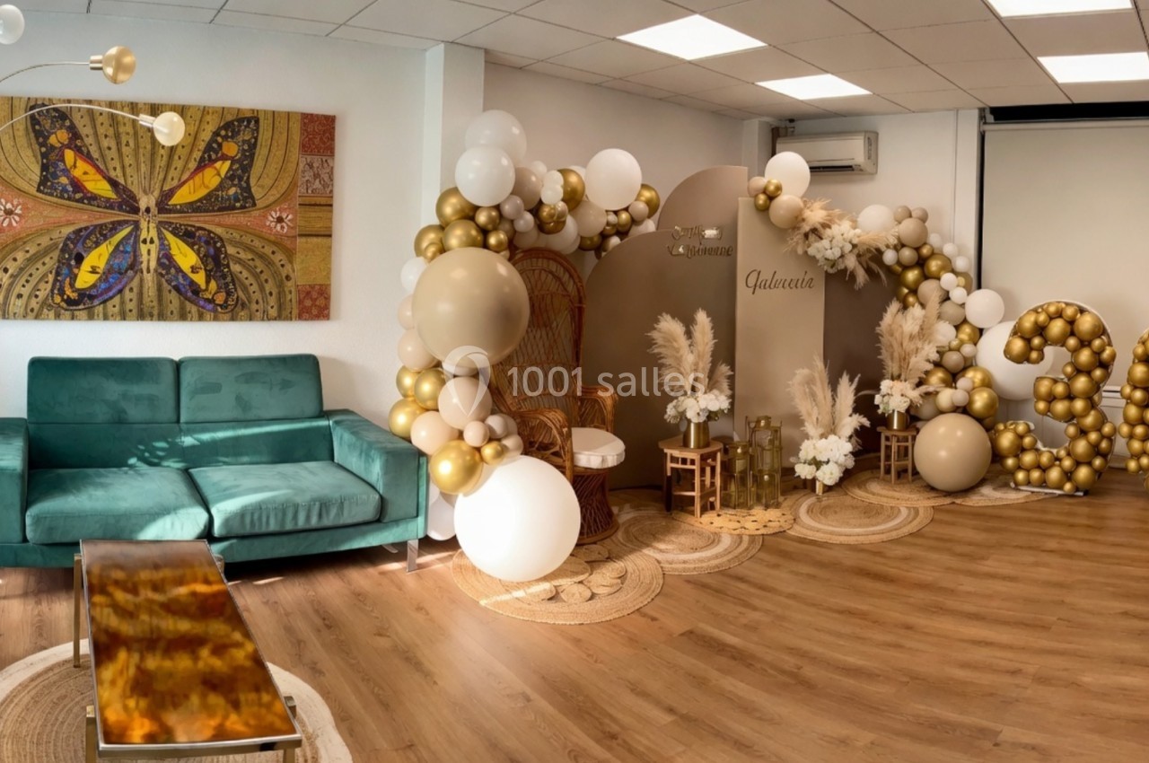 Décoration intérieure avec ballons dorés et blancs formant le chiffre 30, fauteuil en rotin et plantes en arrière-plan.