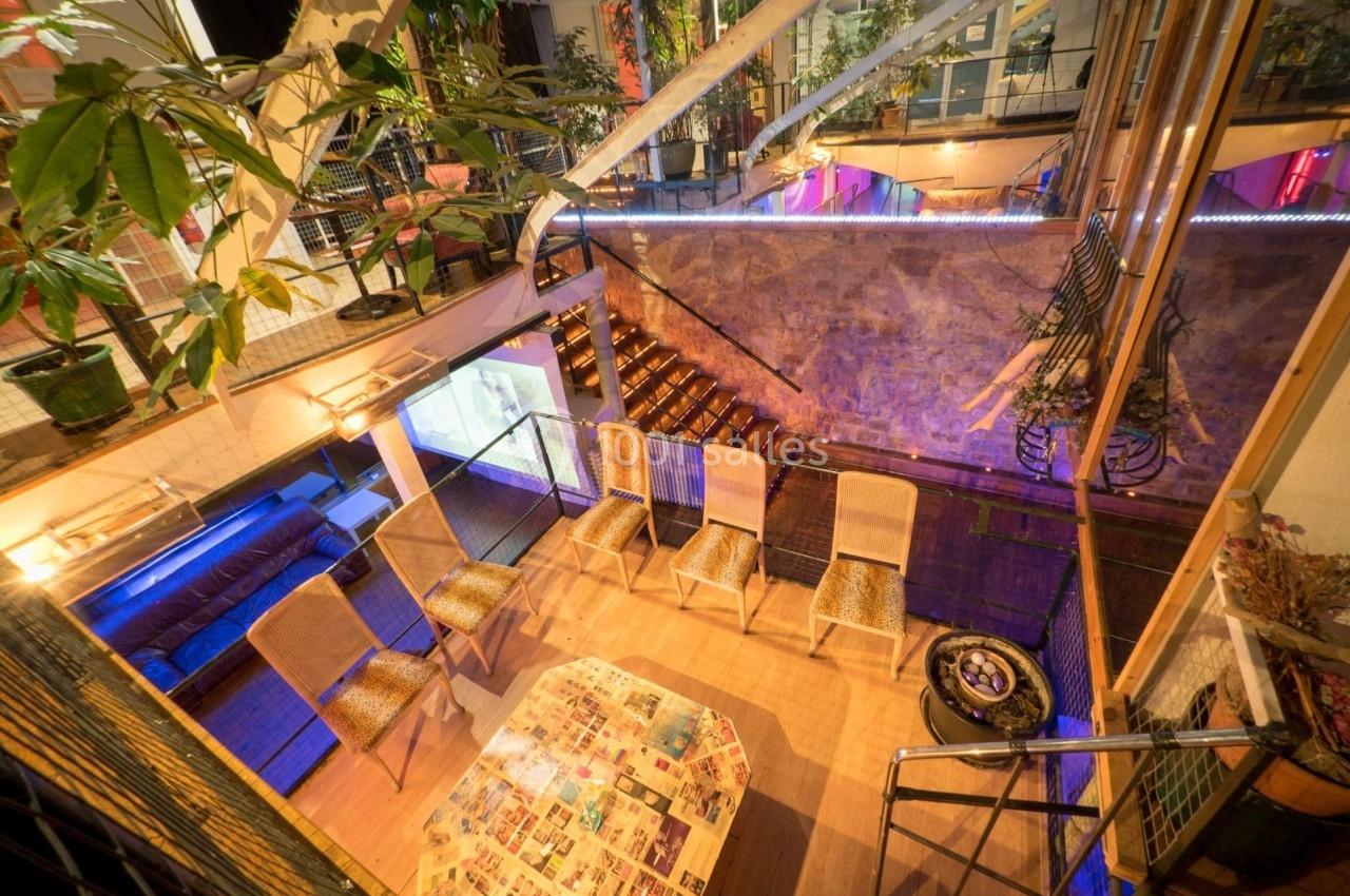 Espace intérieur lumineux avec des chaises disposées autour d'une table basse, entouré de plantes et d'escaliers en bois.