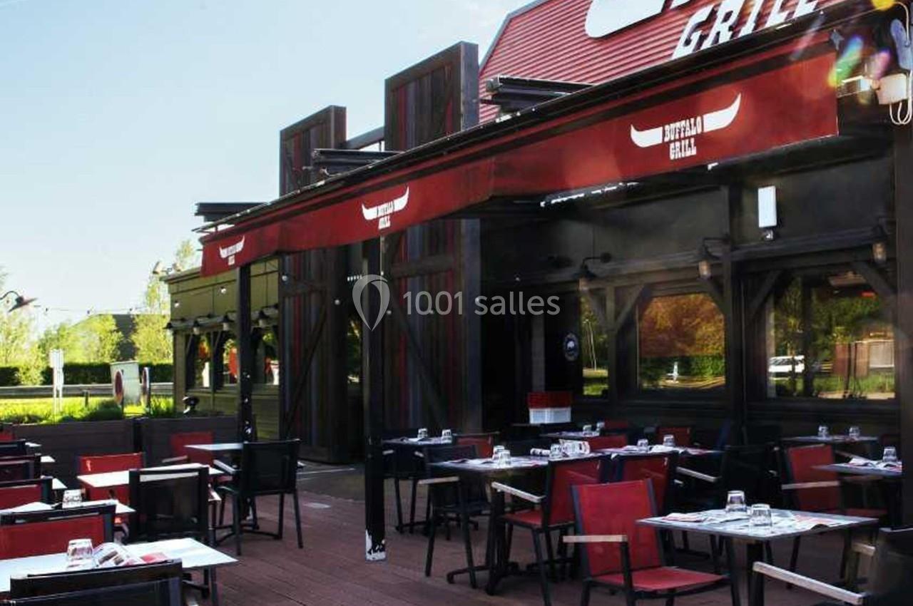 Terrasse extérieure d'un restaurant avec tables dressées, chaises rouges et noires, et auvent rouge.