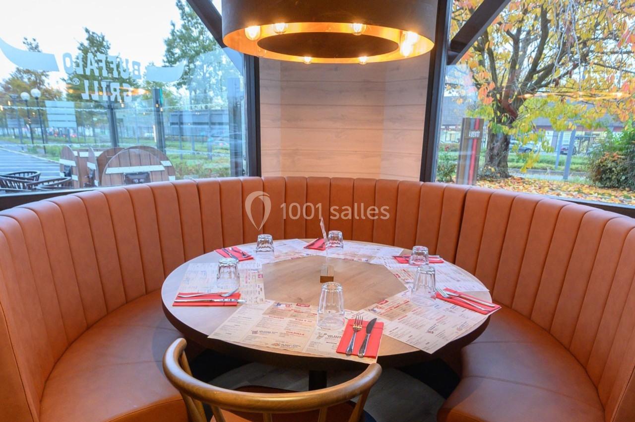 Banquette ronde en cuir marron entourant une table dressée avec des couverts et des verres, éclairée par une suspension.