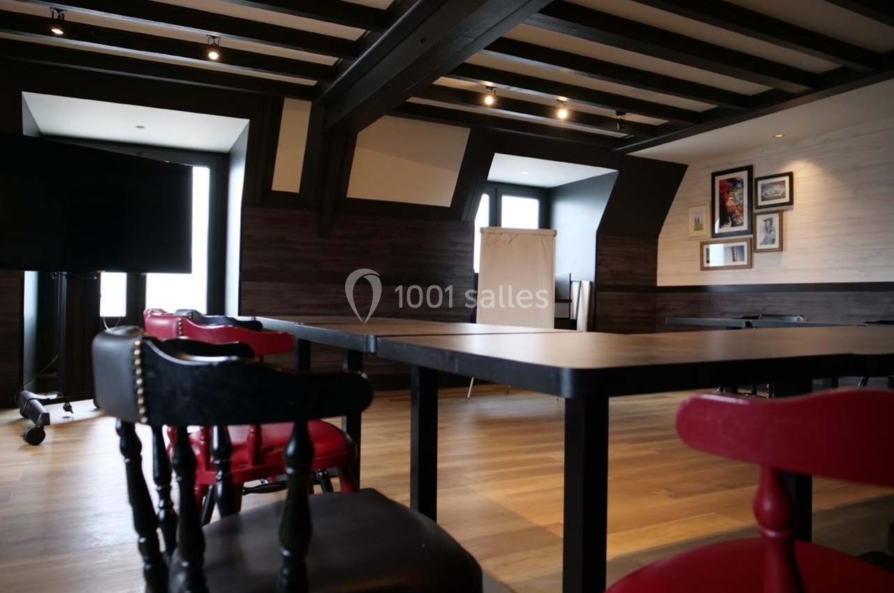 Salle de réunion lumineuse avec tables noires, chaises rouges et noires, tableau blanc et décorations murales.