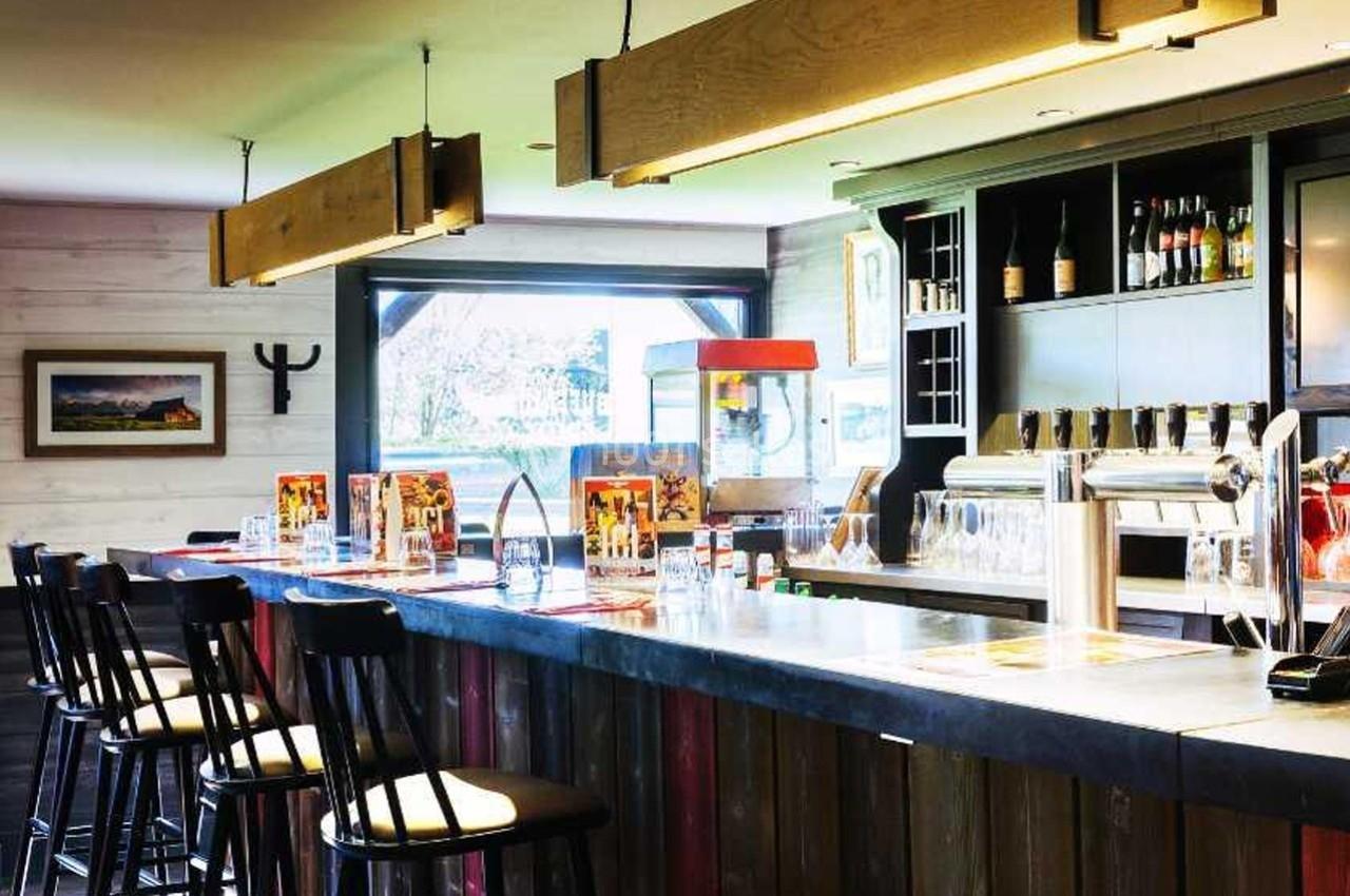 Bar en bois avec tabourets hauts, comptoir équipé de tireuses à bière et étagères contenant des bouteilles à l'arrière.