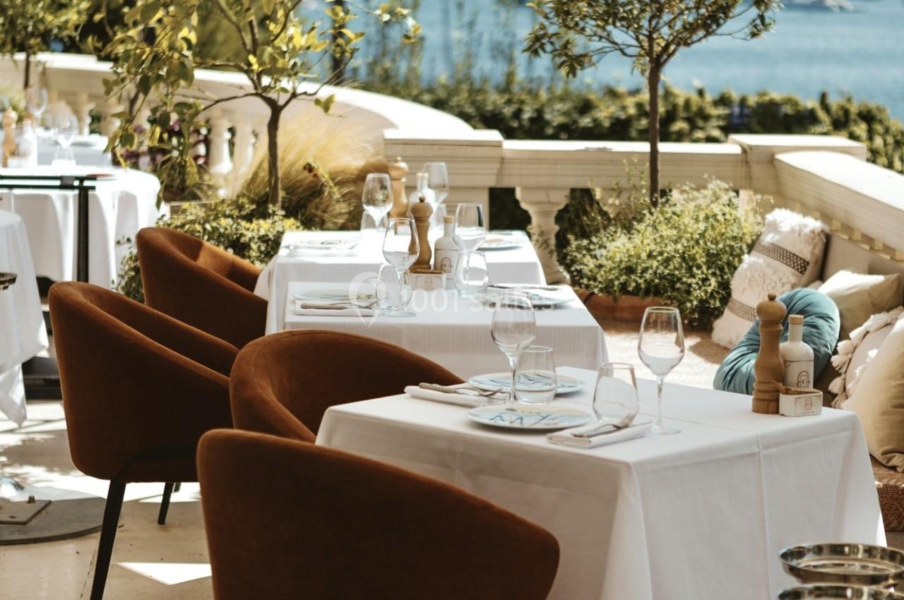 Terrasse d'un restaurant élégamment aménagée avec des tables dressées, chaises confortables et vue sur un paysage ensoleillé.