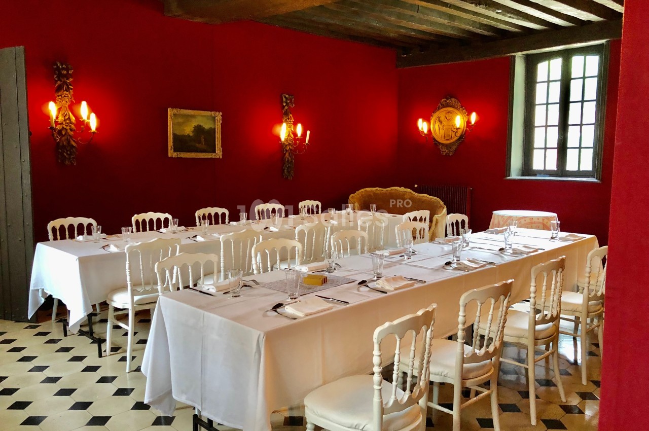 Salle à manger avec murs rouges, tables dressées avec nappes blanches, chaises blanches et sol en damier noir et blanc.