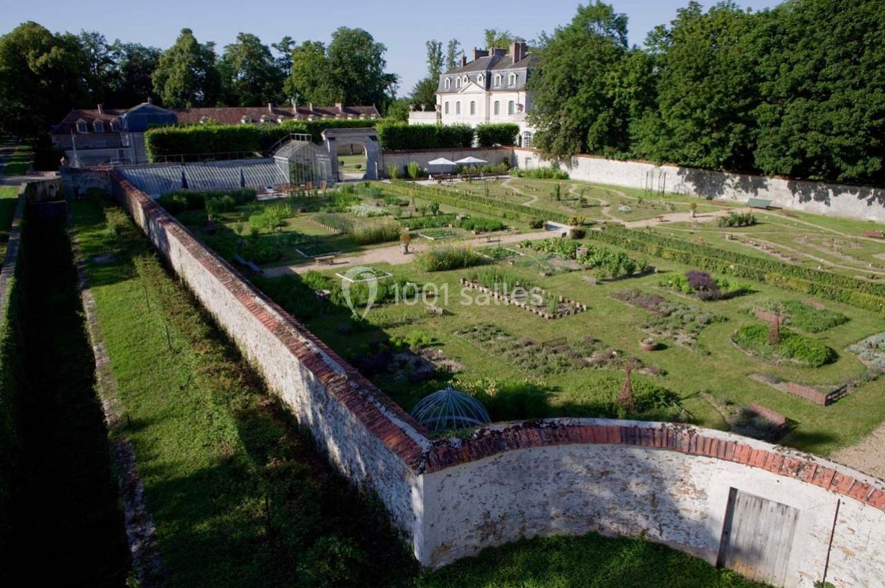Jardin potager clos de murs avec allées symétriques, serres et bâtiment historique en arrière-plan.