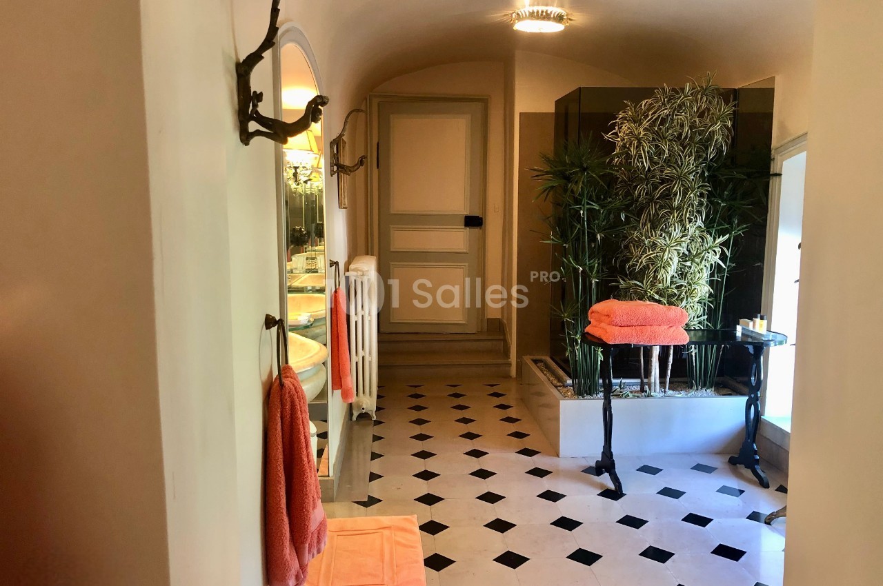 Salle de bain lumineuse avec sol en damier, serviettes orange, plantes vertes et baignoire en arrière-plan.