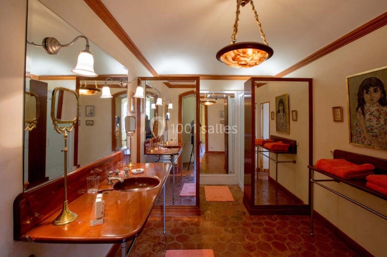 Salle de bain rétro avec lavabo en bois, miroirs, éclairage suspendu et serviettes orange sur des étagères.