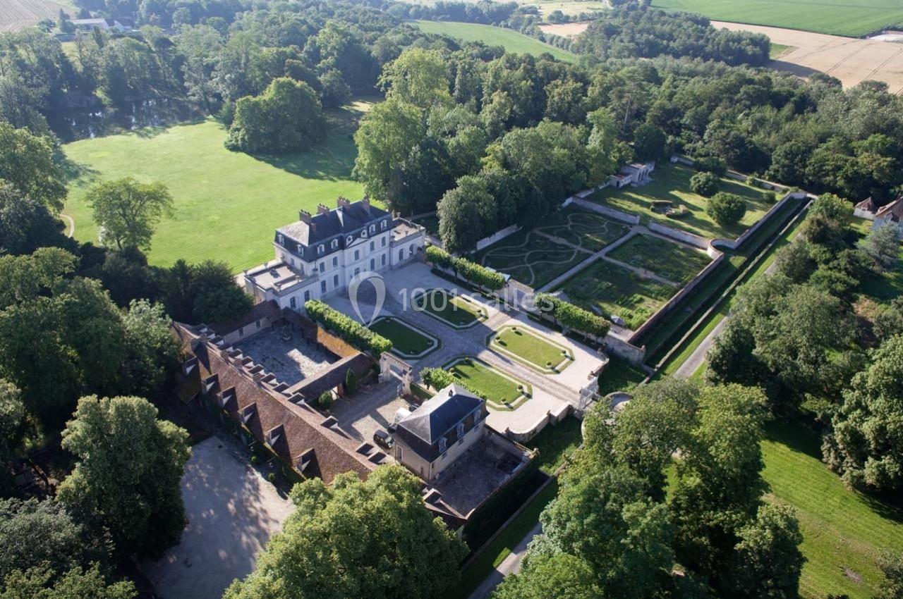 Vue aérienne d'un château entouré de jardins symétriques, d'arbres et de vastes espaces verts en pleine campagne.