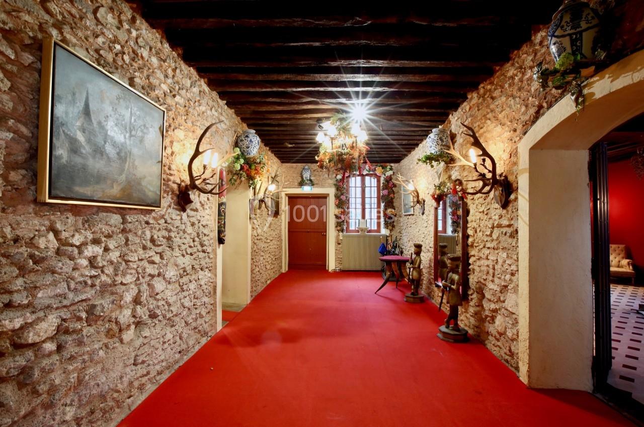 Couloir avec murs en pierre, plafond à poutres apparentes, tapis rouge et décorations murales comprenant des bois de cerf.