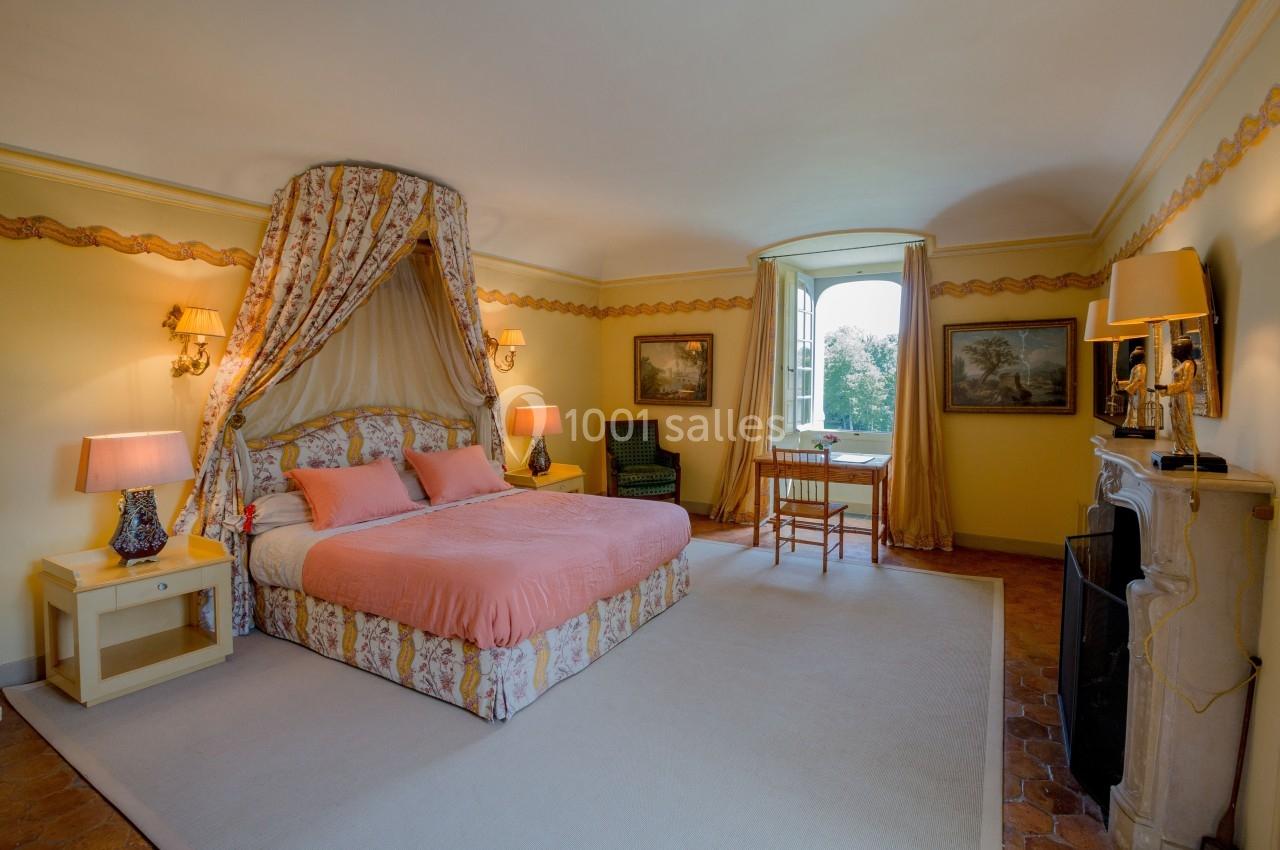 Chambre lumineuse avec lit à baldaquin, murs jaunes, meubles classiques et vue sur un jardin par une fenêtre ouverte.