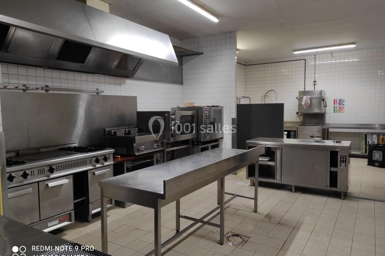 Cuisine professionnelle avec équipements en inox, comprenant fours, plaques de cuisson, plans de travail et évier.