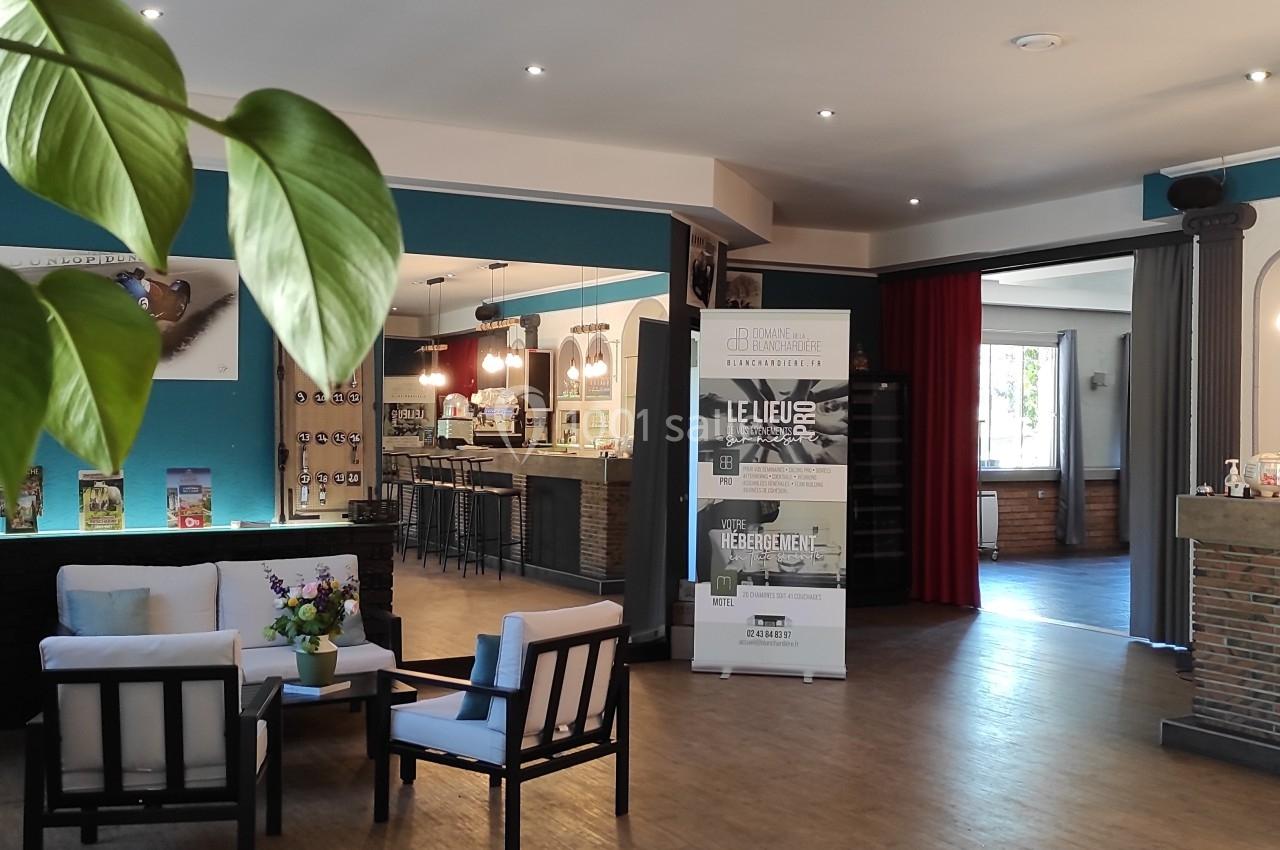 Espace intérieur lumineux avec coin salon, bar en arrière-plan et plantes décoratives au premier plan.