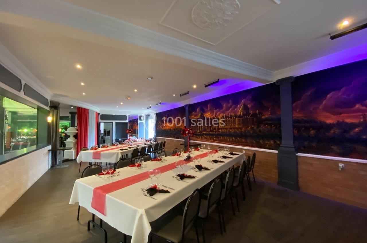 Salle de réception décorée avec des tables dressées, nappes blanches et rouges, et fresque murale en arrière-plan.