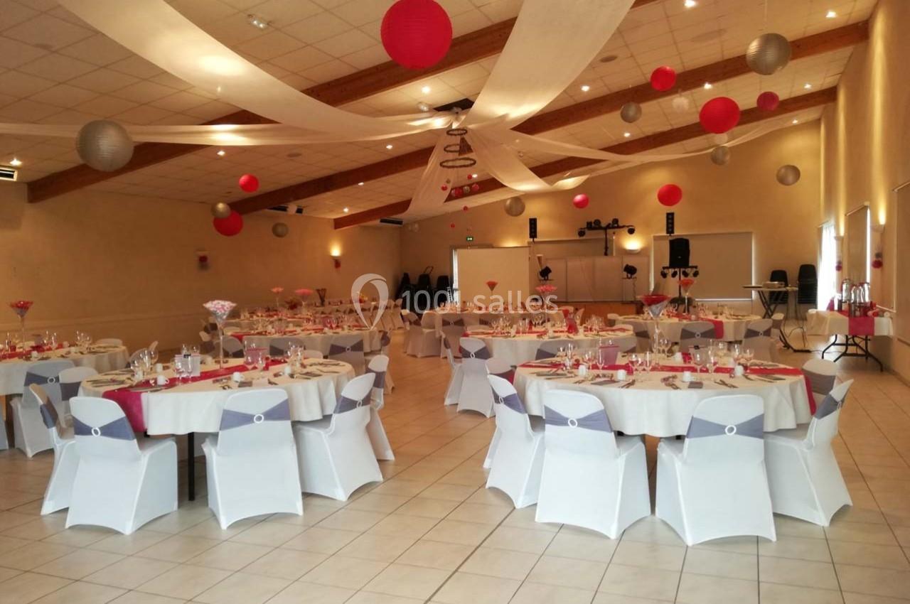 Salle de réception décorée avec des tables rondes dressées, des nappes blanches et des suspensions rouges et grises.