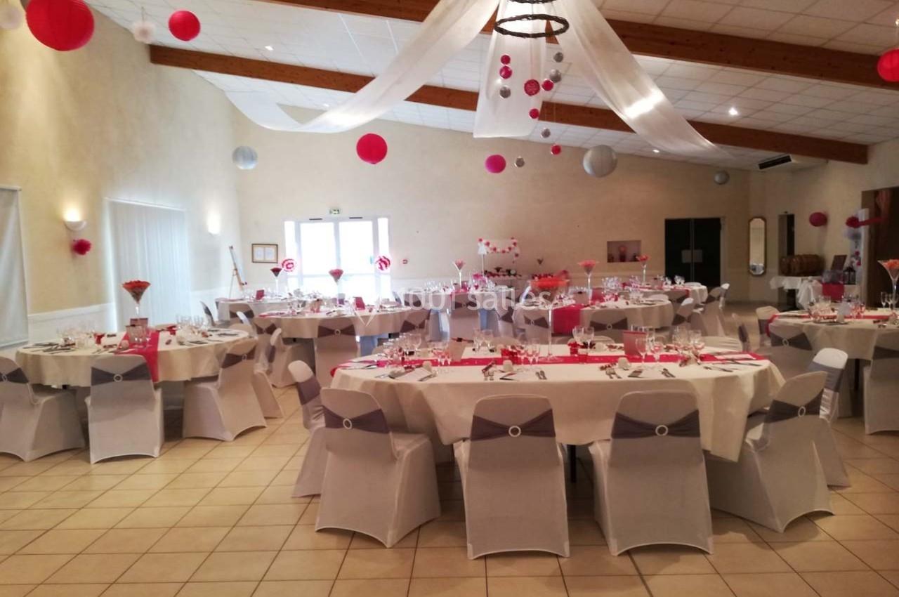 Salle de réception décorée avec des tables rondes, nappes blanches et éléments rouges, prête pour un événement festif.