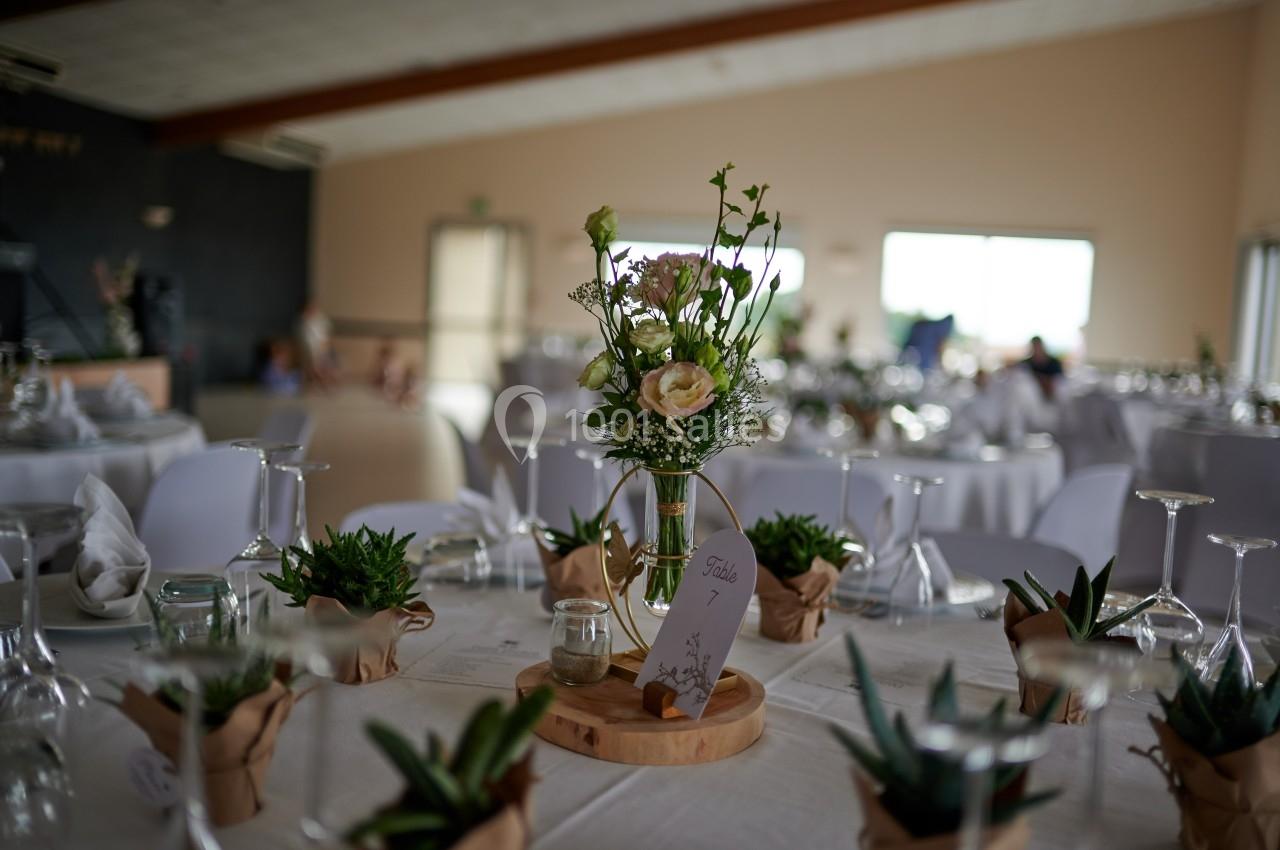 Centre de table avec vase floral et plantes en pot, disposé sur une table dressée dans une salle de réception lumineuse.