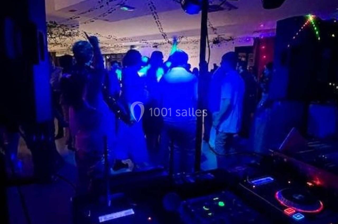 Personnes dansant sous des lumières bleues dans une salle sombre, avec une table de mixage au premier plan.