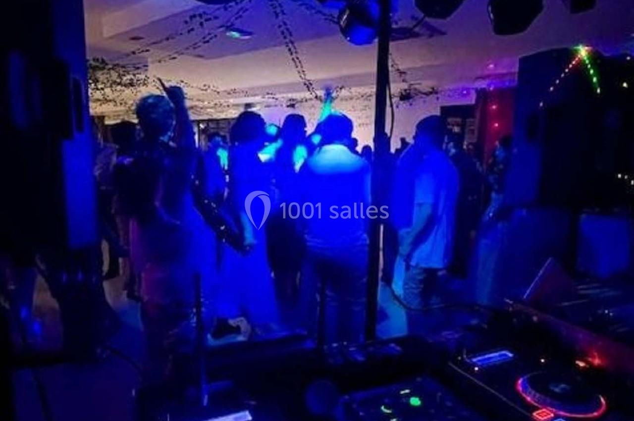 Personnes dansant sous des lumières colorées dans une ambiance festive, avec une table de mixage au premier plan.