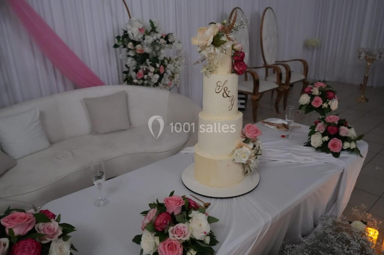 Gâteau de mariage à trois étages décoré de fleurs, posé sur une table ornée de bouquets roses et blanches.