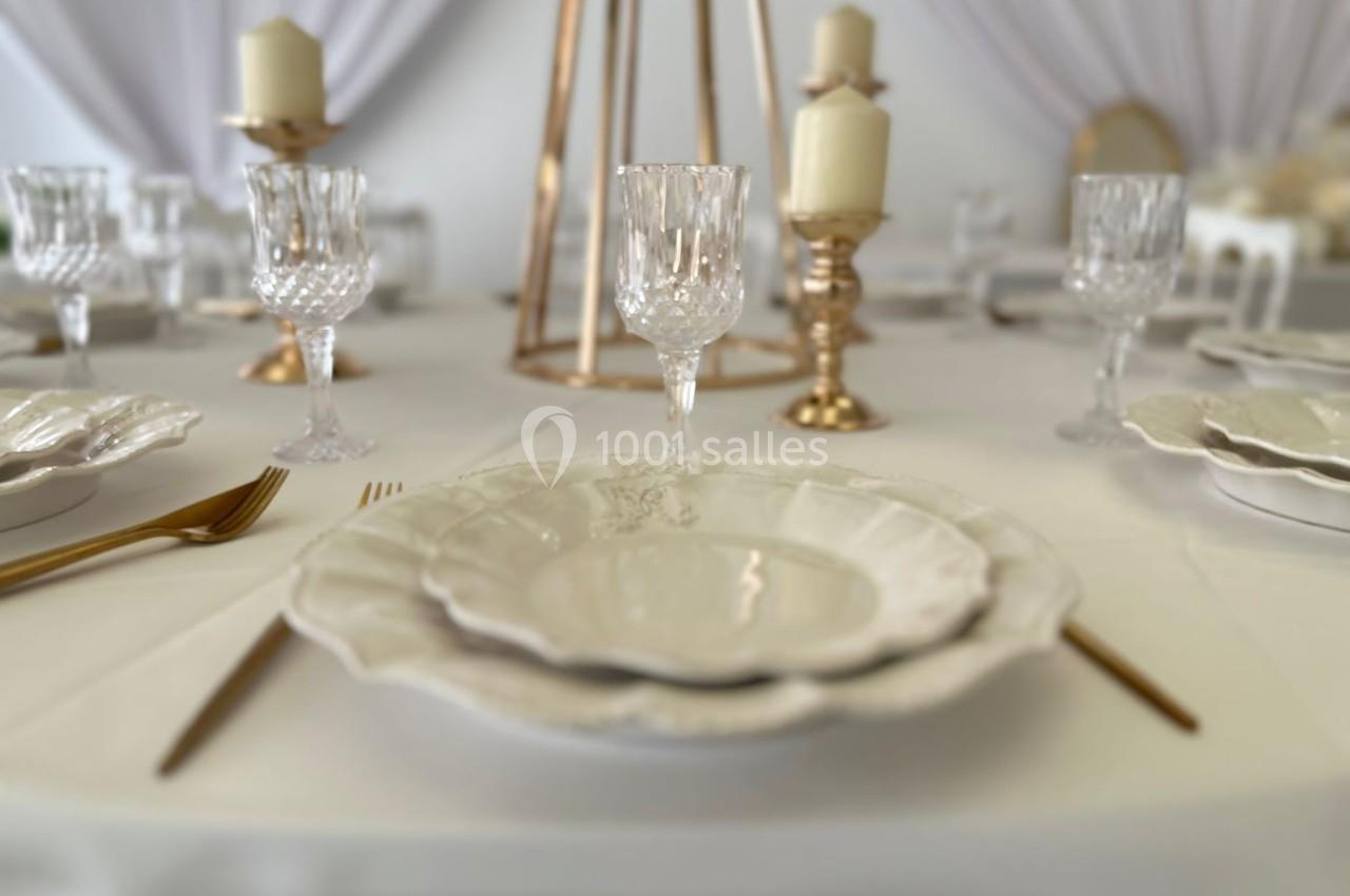 Table élégamment dressée avec vaisselle blanche, verres en cristal, couverts dorés et chandeliers décoratifs.