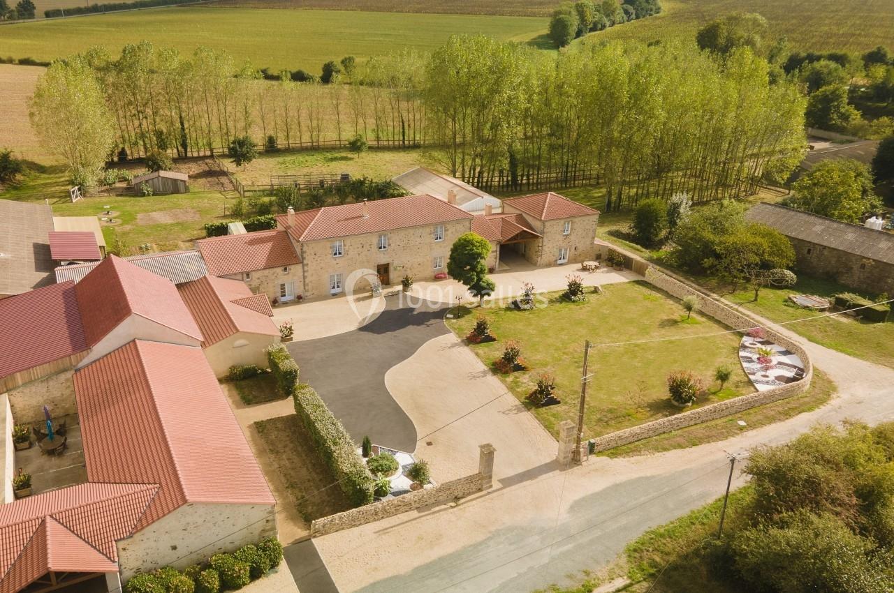 Vue aérienne d'une propriété rurale avec bâtiments en pierre, toits rouges, cour pavée et champs environnants.