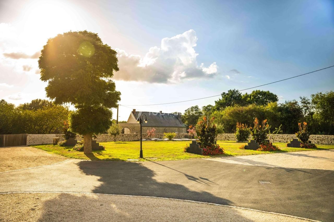 Jardin avec pelouse, parterres fleuris, lampadaire et maison en arrière-plan sous un ciel ensoleillé.