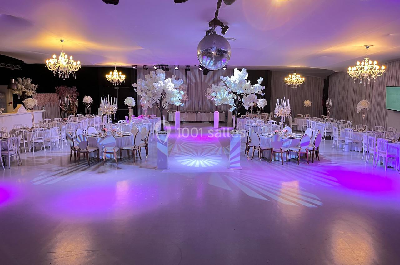 Salle de réception élégante avec tables décorées, éclairage coloré et une piste de danse sous une boule à facettes.