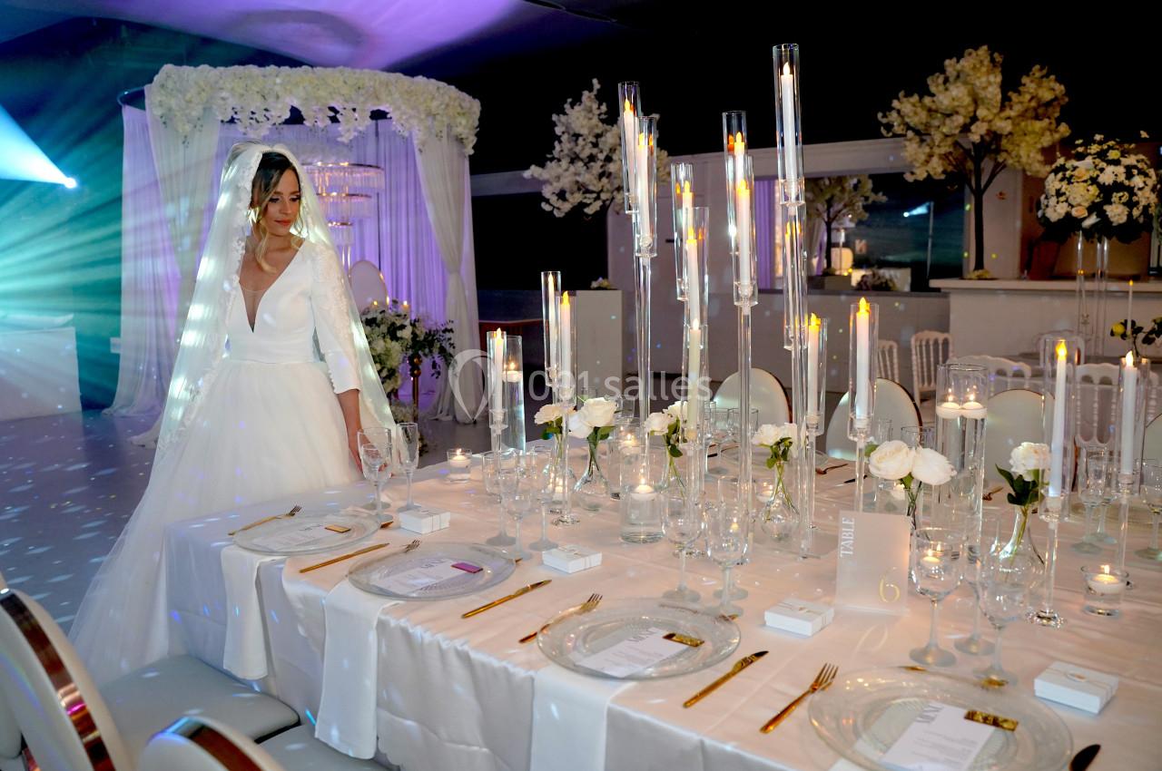 Une mariée en robe blanche observe une table de réception élégamment décorée avec des bougies et des fleurs blanches.