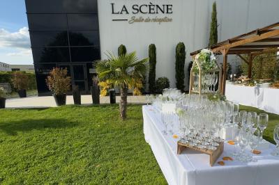 Façade d'un bâtiment moderne éclairé de nuit, avec des plantes et un panneau ’La Scène’ visible.