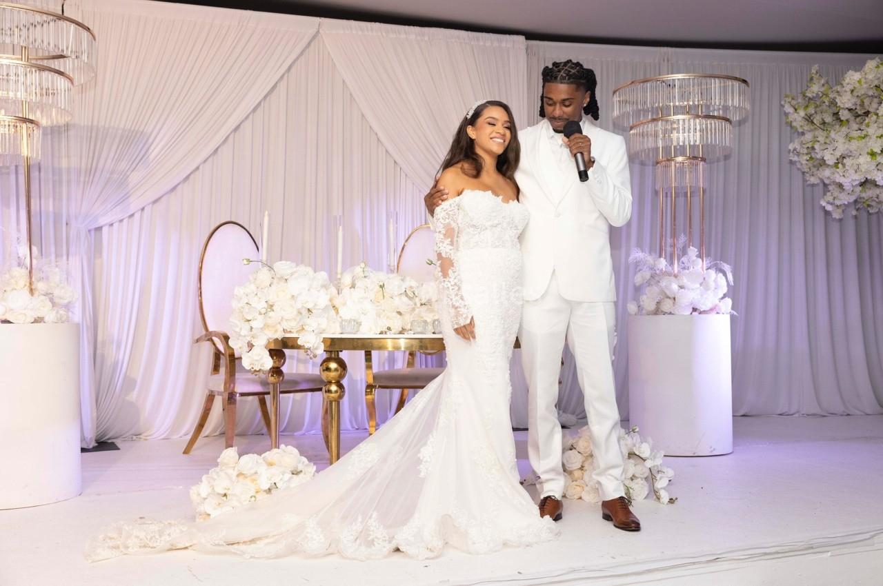 Un couple en tenue de mariage pose devant une table décorée de fleurs blanches dans une salle élégante.