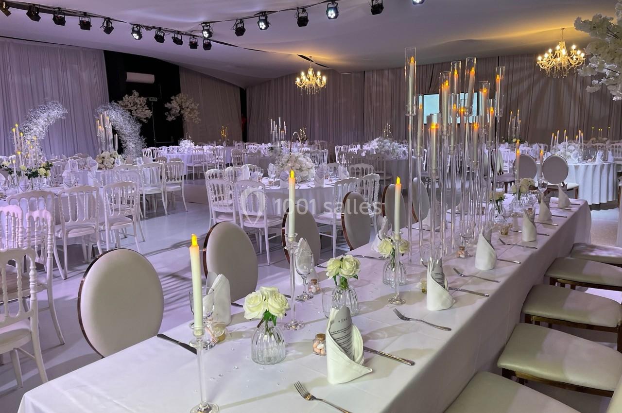 Salle de réception décorée pour un mariage, avec tables élégantes, chandeliers et fleurs blanches.