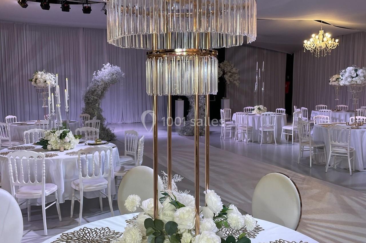 Centre de table élégant avec fleurs blanches, bougie dorée et lustre en cristal dans une salle de réception décorée.
