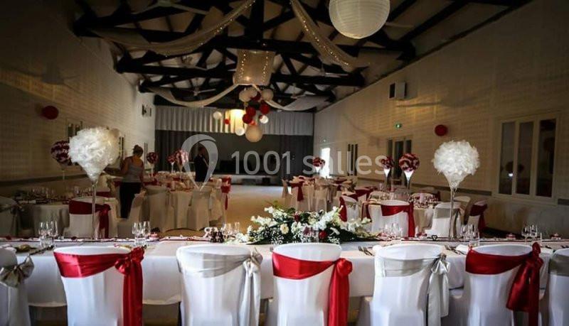 Salle de réception décorée avec des tables dressées, chaises ornées de rubans rouges et centres de table élégants.