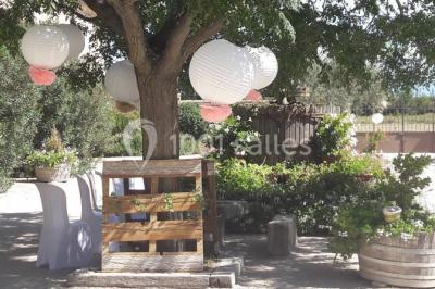 Bâtisse provençale entourée de cyprès et de champs verts, avec des arbres en arrière-plan sous un ciel clair.