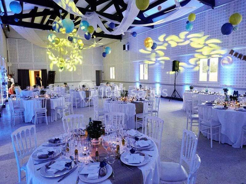 Salle de réception décorée avec des tables dressées, des guirlandes lumineuses et des suspensions colorées au plafond.