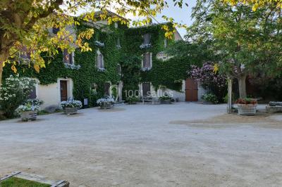 Bâtisse provençale entourée de cyprès et de champs verts, avec des arbres en arrière-plan sous un ciel clair.