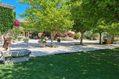 Bâtisse provençale entourée de cyprès et de champs verts, avec des arbres en arrière-plan sous un ciel clair.