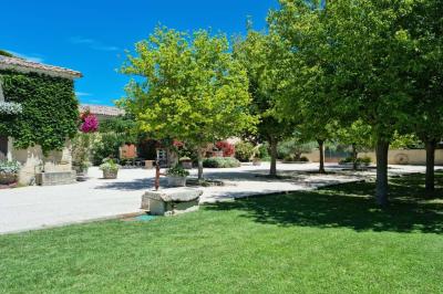 Bâtisse provençale entourée de cyprès et de champs verts, avec des arbres en arrière-plan sous un ciel clair.