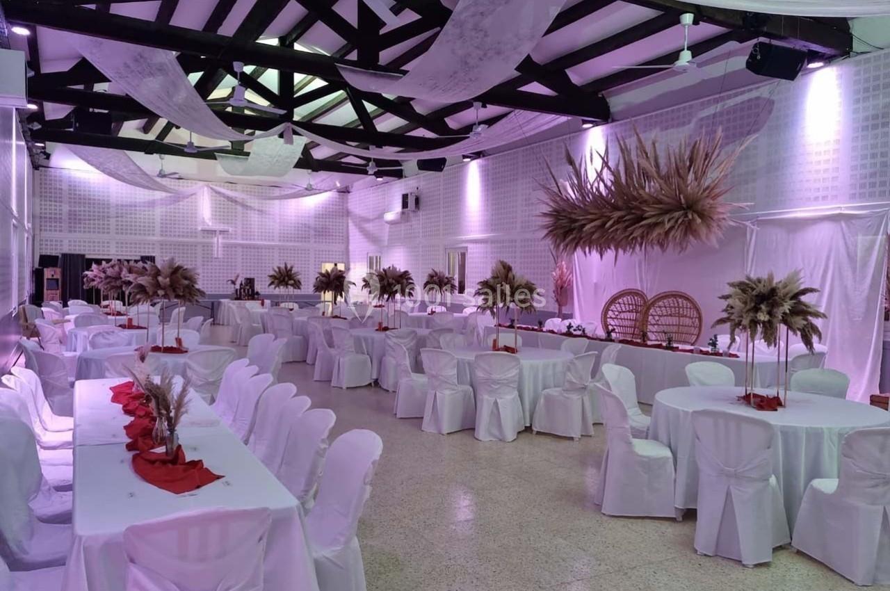 Salle de réception décorée avec des tables blanches, des nappes rouges et des arrangements de fleurs séchées.