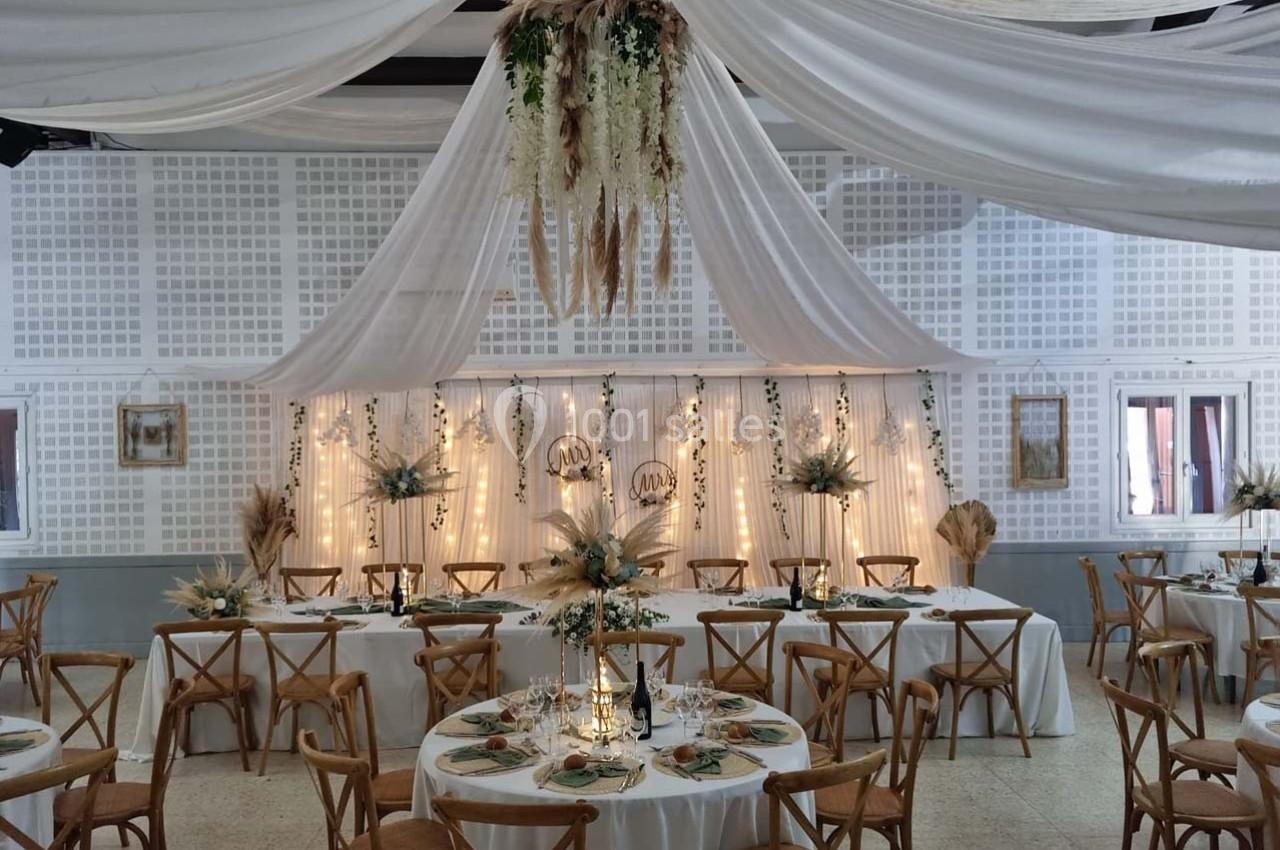 Salle de réception décorée avec des tables rondes, des chaises en bois et des drapés blancs suspendus au plafond.